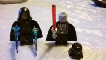 Emperor has grey, wrinkled head. Darth Vader has grey scarred head and comes with a lightsaber.